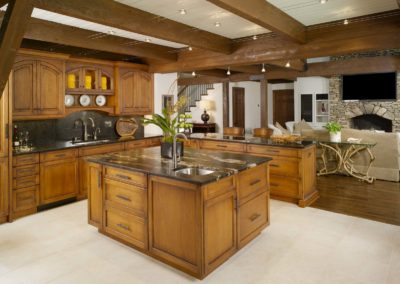 View of Lodge kitchen facing great room, with butternut cabinets, leathered granite island, and lighting wired through the beams