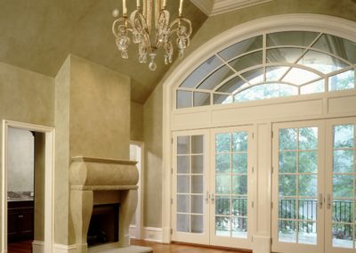 Bedroom with hardwood floors and wood-burning limestone fireplace, chandelier, and double-pane glass doors leading to a balcony.