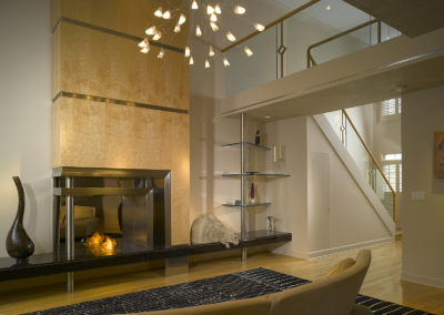 Contemporary living room with ethanol burning fireplace, bird's eye maple face and stainless steel inserts on black granite hearth, plus artistic chandelier and glass pane railing